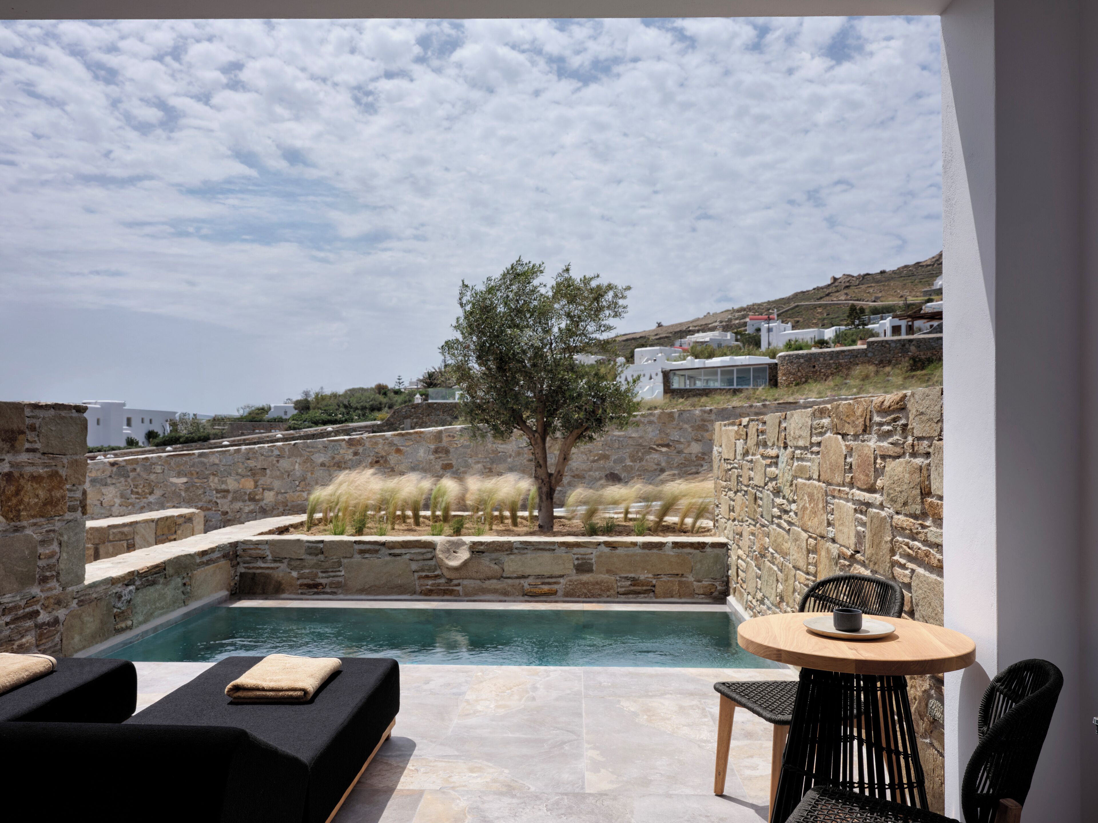 A pool area with stone walls, a wooden table, and black wicker chairs.