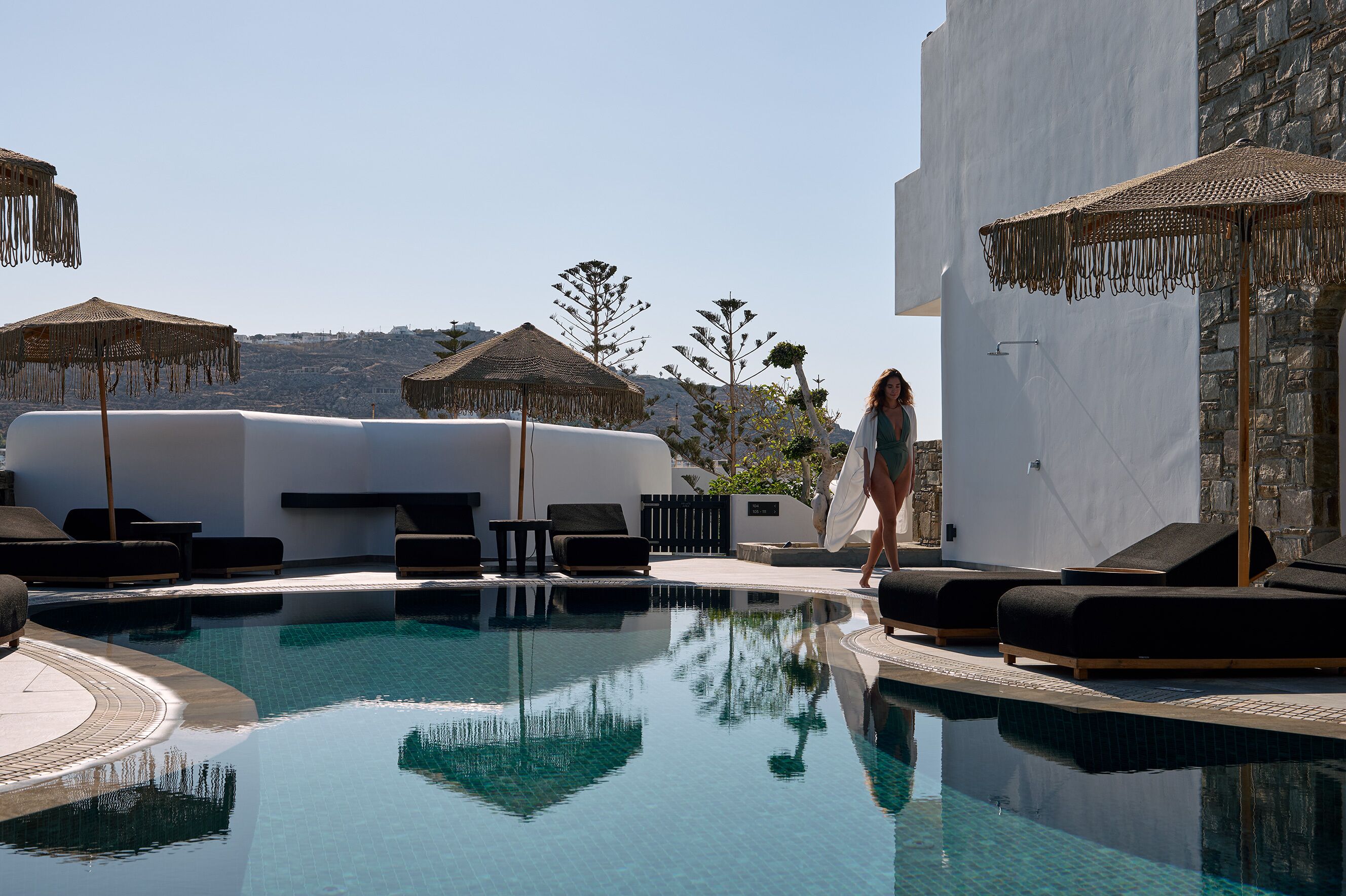 A pool area with lounge chairs and umbrellas, surrounded by white walls and a stone building.