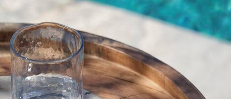 Een glas water op een houten dienblad bij een zwembad.