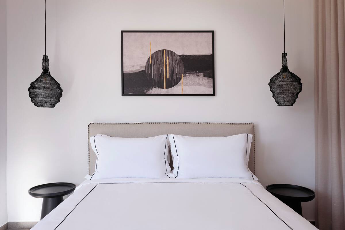A modern bedroom with a large bed, two bedside tables, and a framed abstract artwork on the wall.