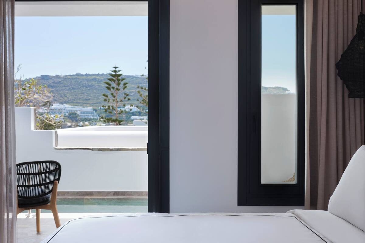 A modern bedroom with a large bed, a chair, and a view of a hillside.