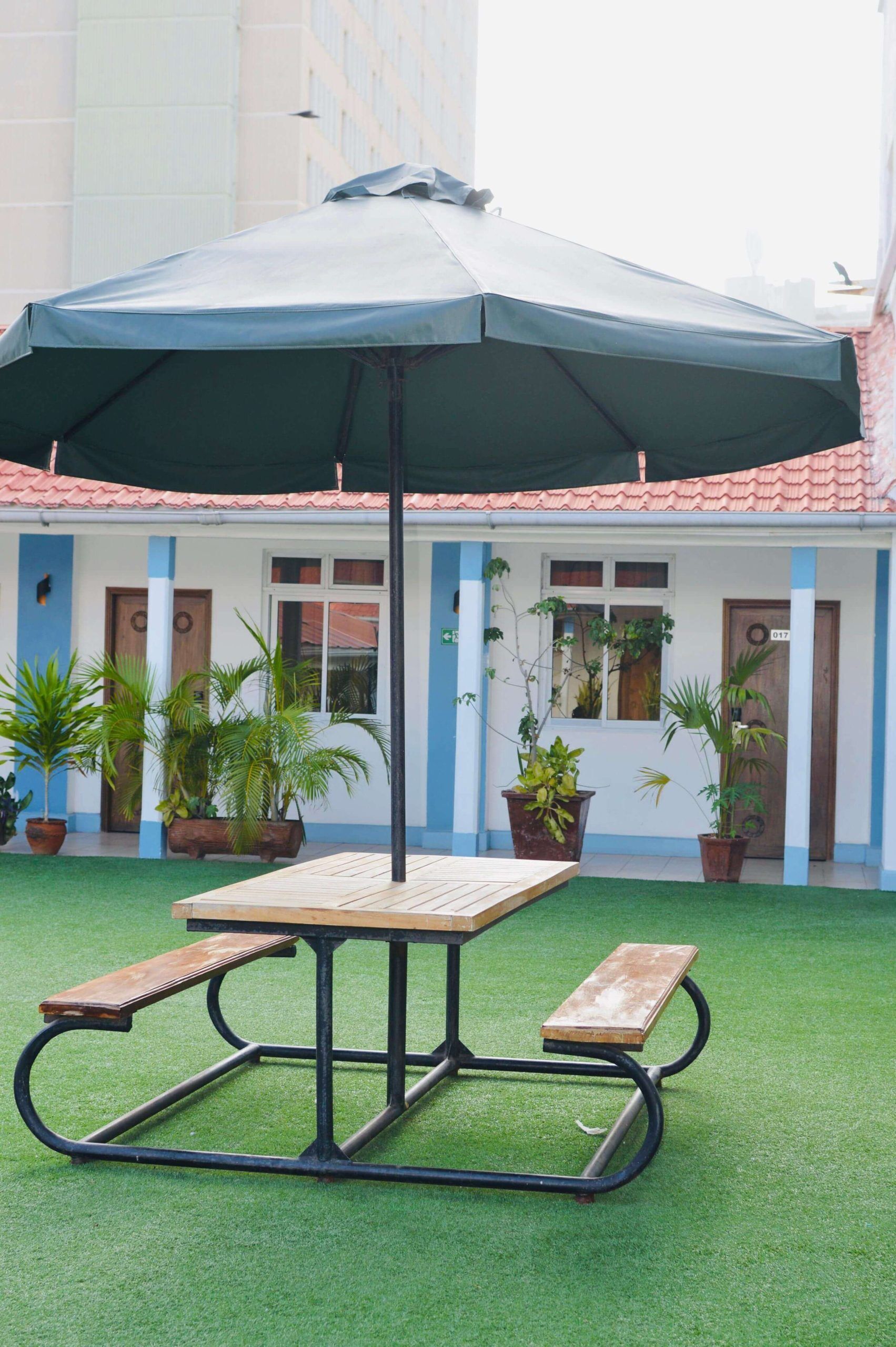 A picnic table with a canopy, surrounded by potted plants, in a courtyard with a building in the background.