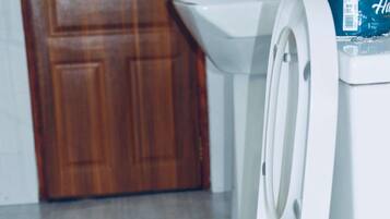 A white toilet with a lid, a wooden door, and a white sink in the background.