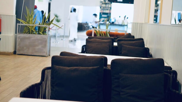 Un restaurante con una barra larga y varias sillas color café con cojines. Se ven plantas en macetas y un extintor.