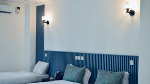 Habitación de hotel con dos camas, un cabecero azul y una lámpara fijada a la pared.