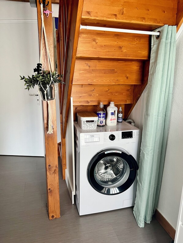 A compact laundry room with a washing machine, a drying rack, and a small shelf with cleaning supplies.