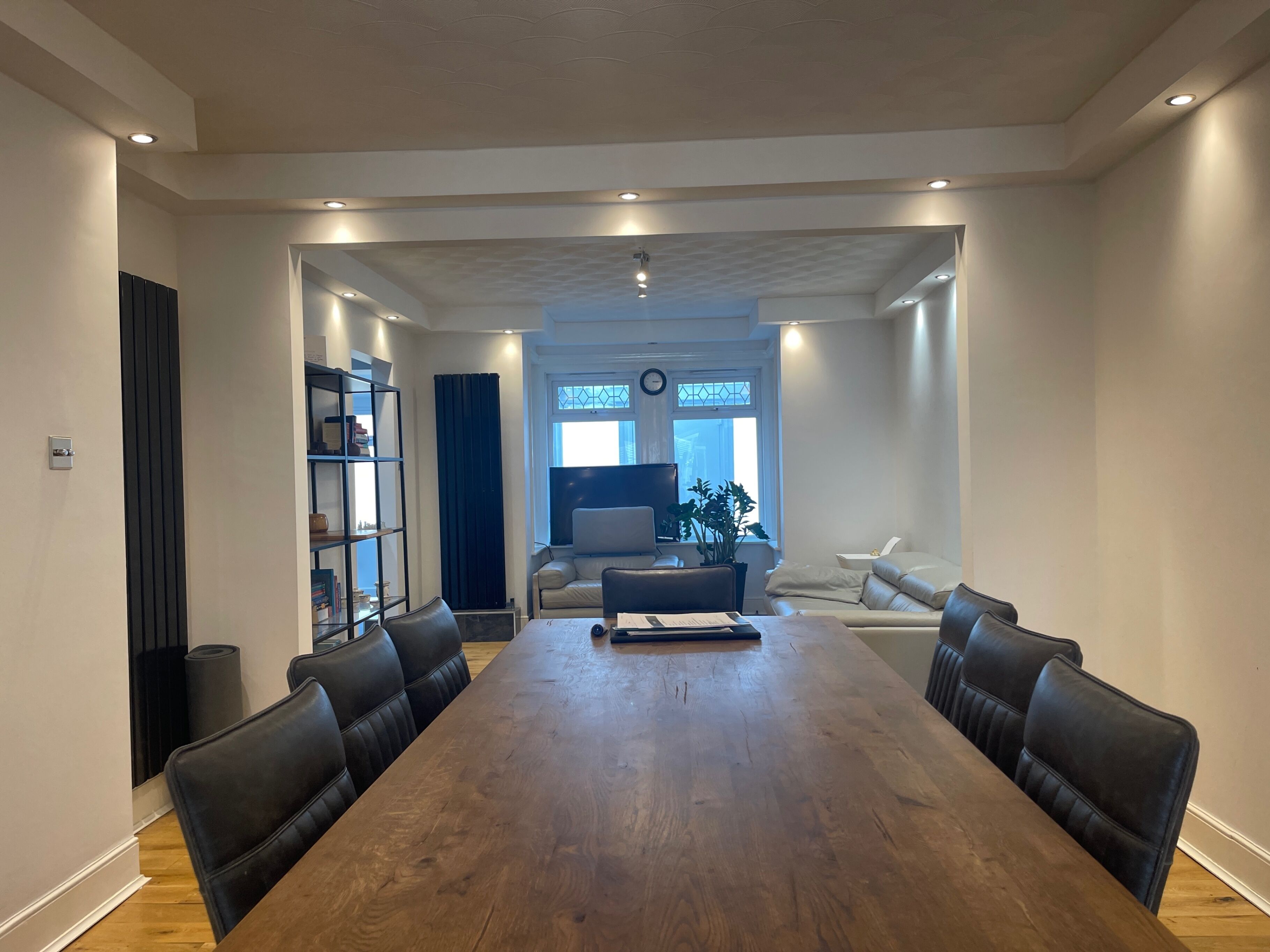 Un salon spacieux avec une grande table à manger en bois, des chaises en cuir noir, un canapé et un téléviseur.