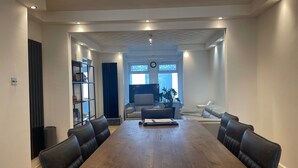 Un salon spacieux avec une grande table à manger en bois, des chaises en cuir noir, un canapé et un téléviseur.