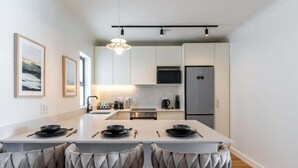 A modern kitchen with white cabinetry, a central island with seating, and a stainless steel refrigerator.