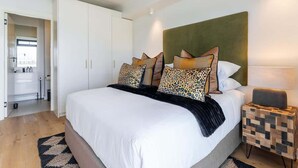 A modern bedroom with a large bed, a headboard, and a bedside table with a lamp.