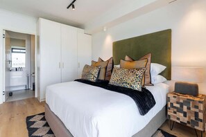 A modern bedroom with a large bed, a headboard, and a bedside table with a lamp.