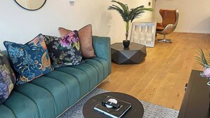 A modern living room with a teal sofa, a coffee table with a remote control, a potted plant, and a modern chair.
