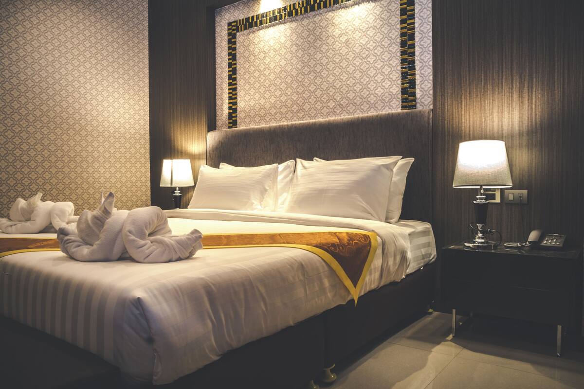 A hotel room with a neatly made bed, a bedside lamp, a telephone, and a wall with a patterned wallpaper.