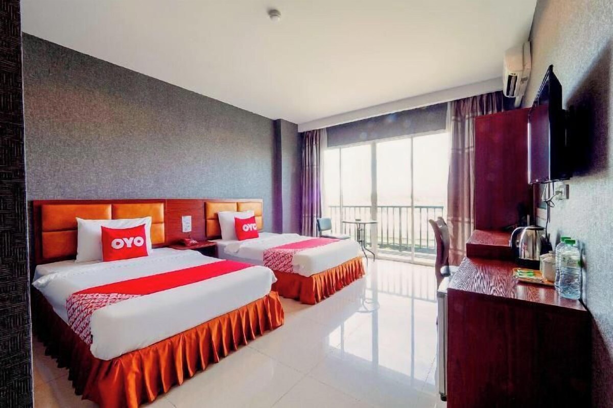 Habitación de hotel con dos camas, un escritorio, televisor y balcón.