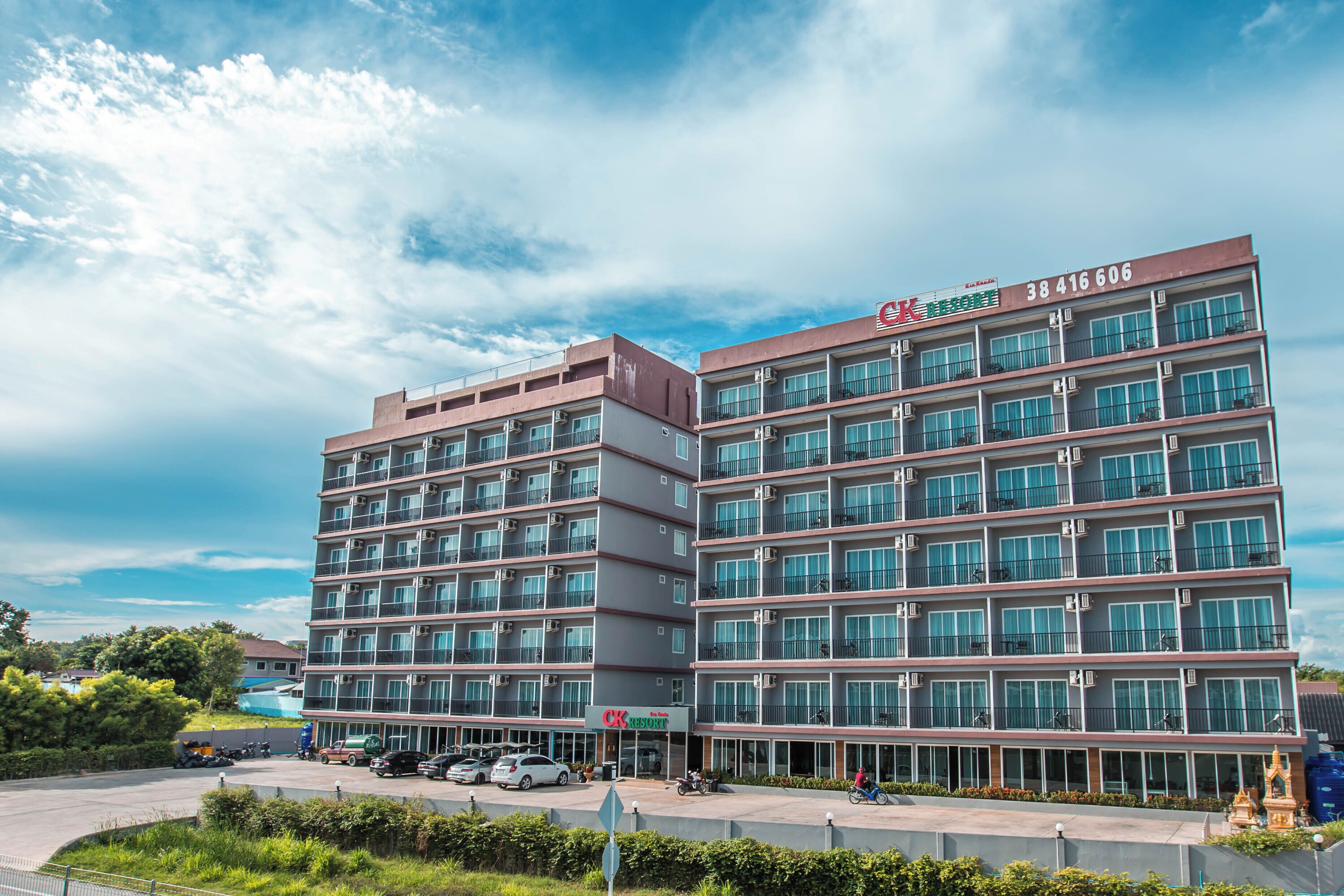 A multi-story hotel with balconies, a parking area, and a clear sky.