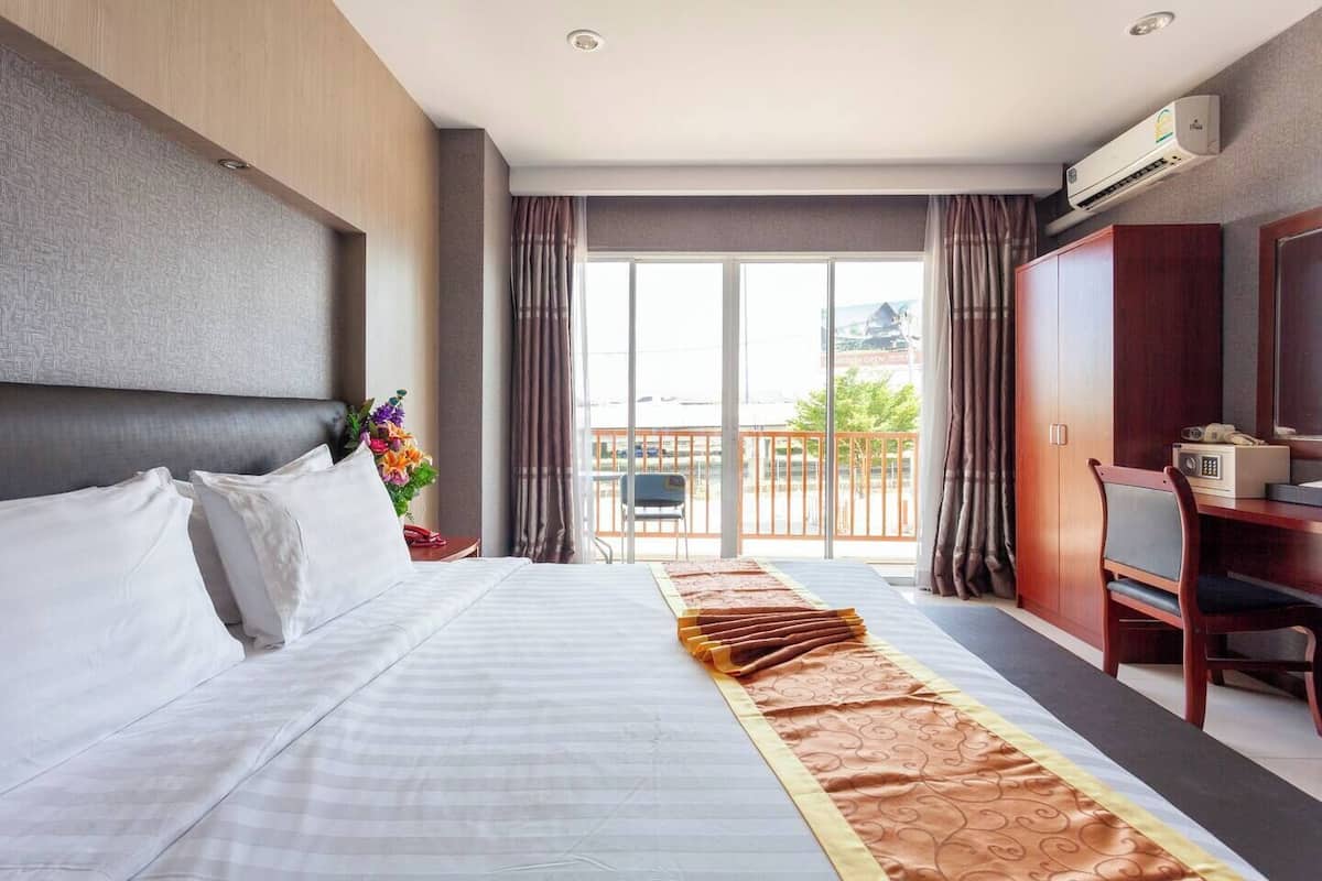 A hotel room with a large bed, a desk with a chair, a wardrobe, and a balcony with a view.