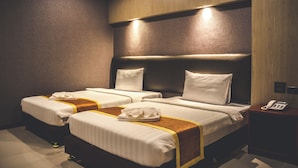 A hotel room with two beds, a wooden headboard, a bedside table with a phone, and a wall-mounted light.