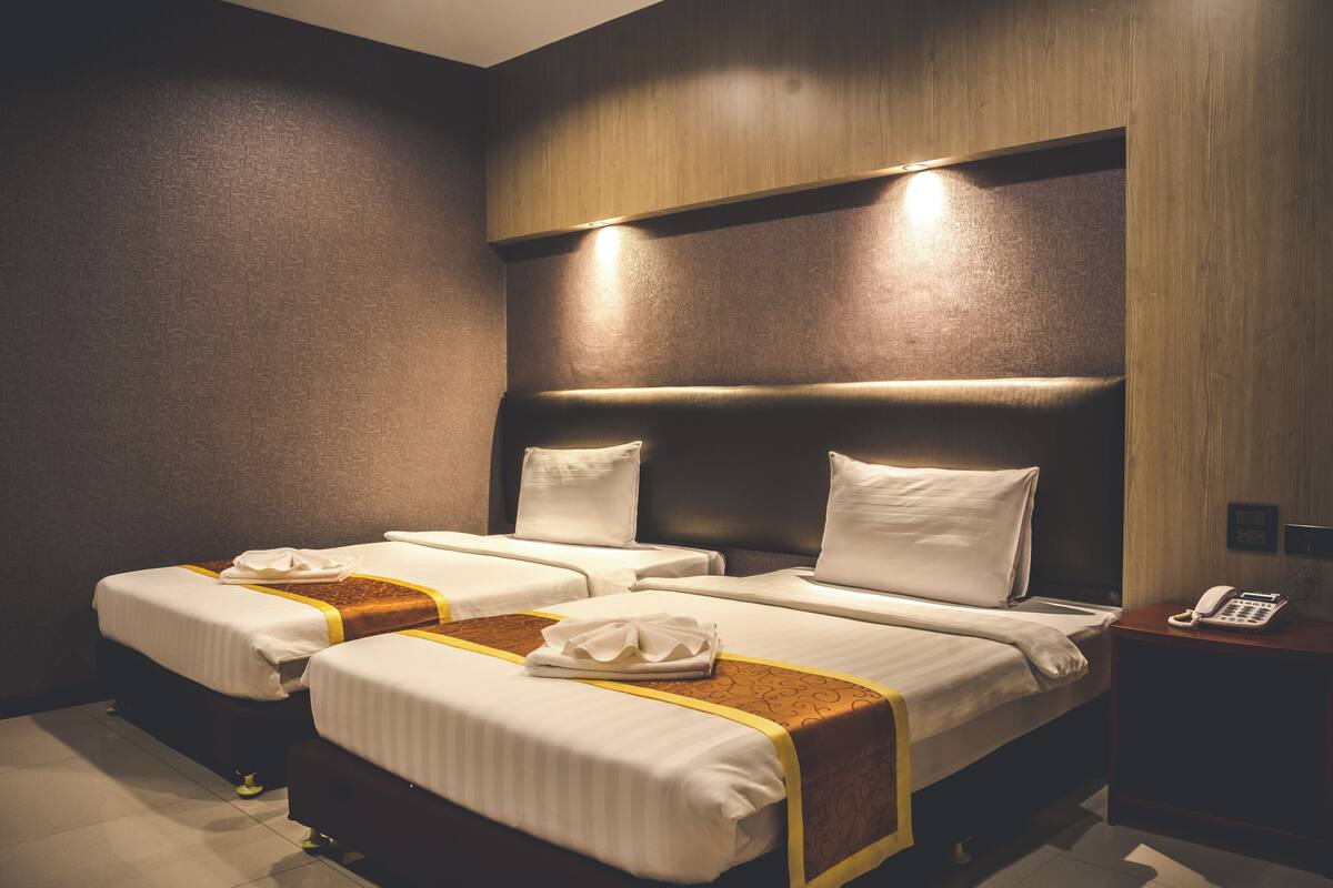 A hotel room with two beds, a wooden headboard, a bedside table with a phone, and a wall-mounted light.