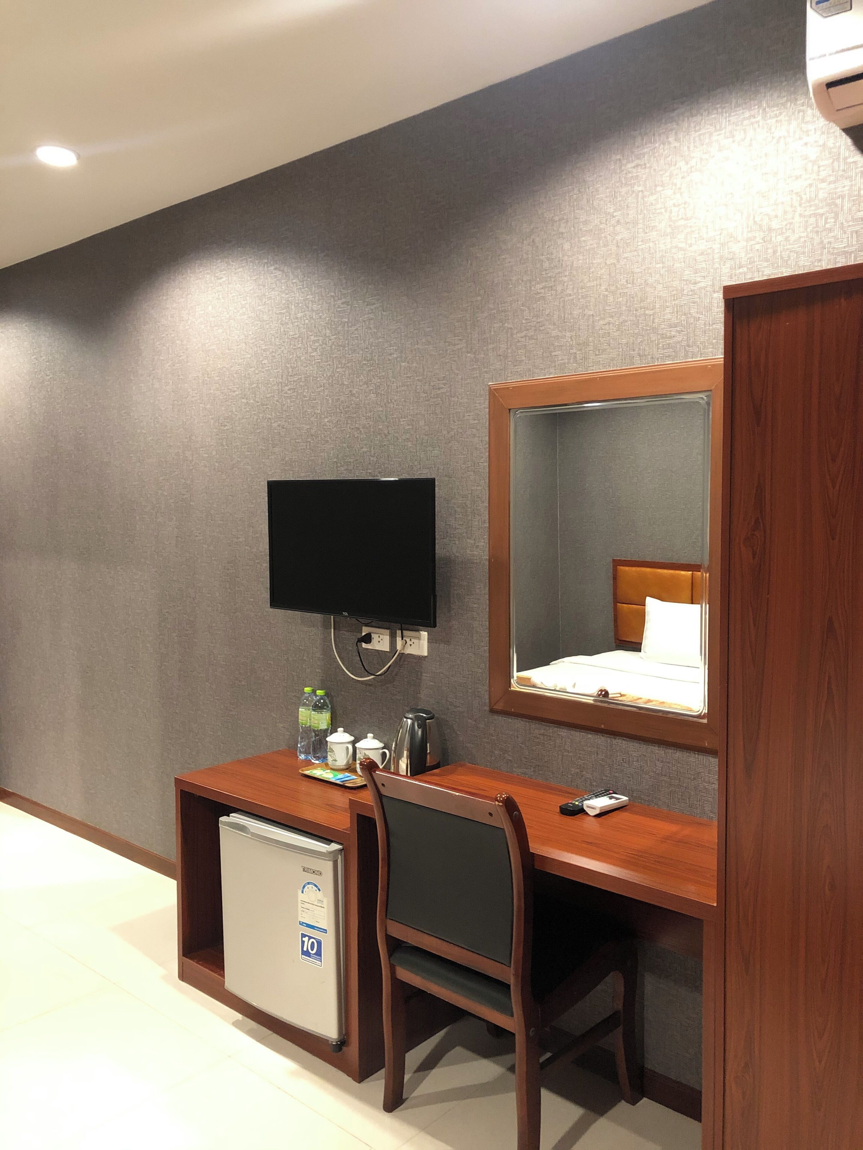 Habitació d'hotel amb escriptori de fusta, una cadira, nevera petita, televisió de pantalla plana penjada a la paret i un mirall gran sobre el llit.