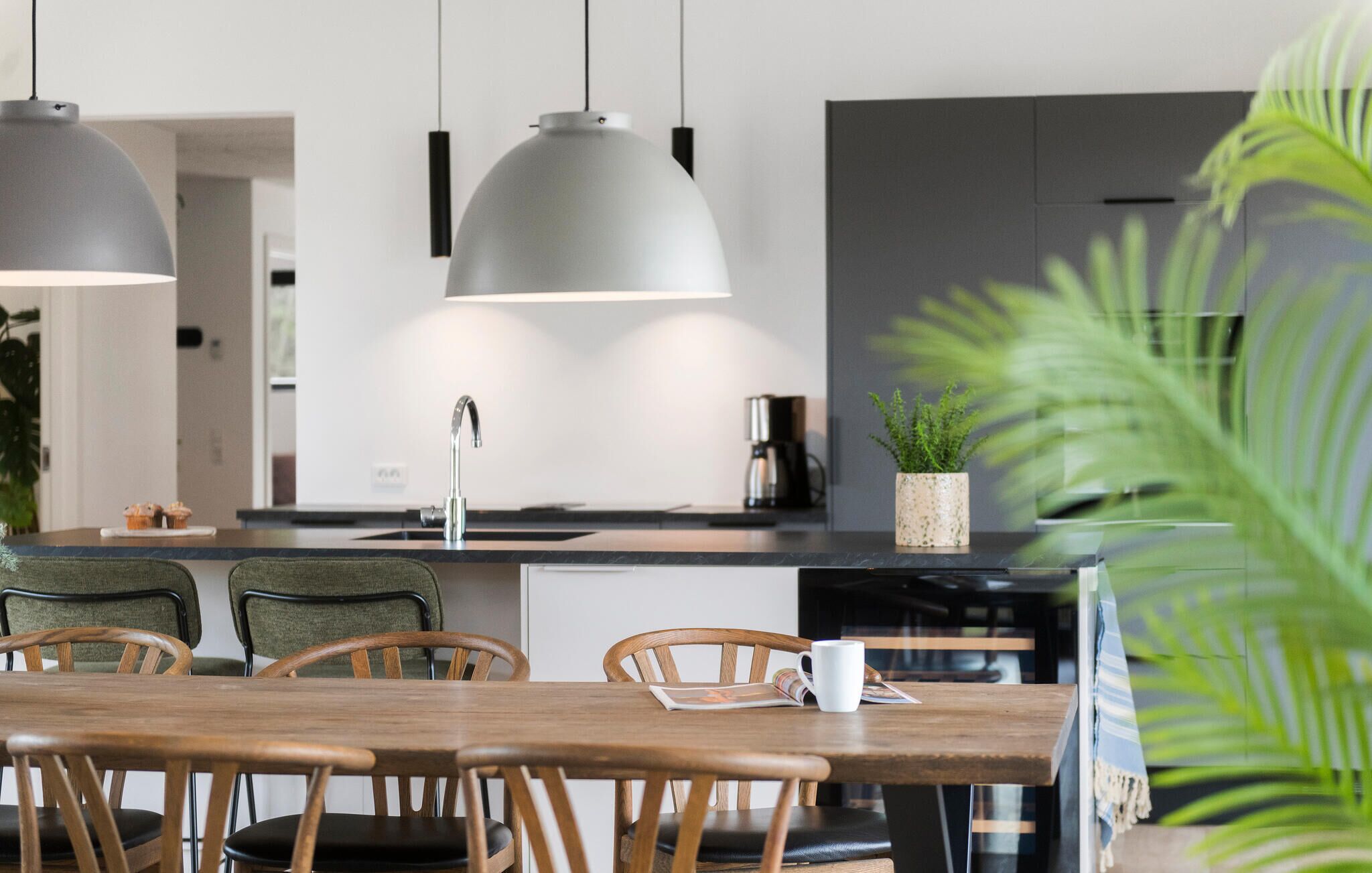 A modern kitchen with pendant lighting, a coffee machine, and a dining area with wooden chairs and a table.