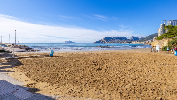 A beach with a clear sky, a sandy shore, and a distant mountain range. - Inftour Apolo III Atico (Calp)