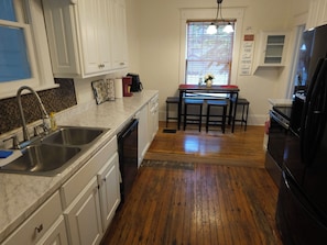 A kitchen with white cabinets, a double sink, a dishwasher, a dining table with chairs, and a refrigerator. - Charming 4-Bedroom Historic Home w/ Game Room + Backyard BBQ (Goldsboro)