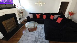 Een woonkamer met een zwarte modulaire bank, een glazen salontafel, een open haard en een modern kunstwerk aan de muur.