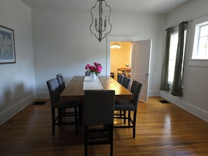 A dining room with a wooden table, six chairs, a vase with flowers, and a chandelier. - Charming 4-Bedroom Historic Home w/ Game Room + Backyard BBQ (Goldsboro)