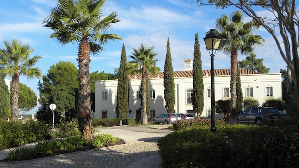 A building with a cobblestone driveway, palm trees, and parked cars. - 3Br Apt-quinta do Lago-private Terrace (Loulé)
