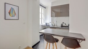 A modern kitchen with a bar counter, two stools, and a large window. - Le Recollet - Versailles (Versailles)