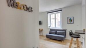 A modern living room with a grey sofa, a dining area with a table and chairs, a large window, and a 'Welcome' sign on the wall. - Le Recollet - Versailles (Versailles)