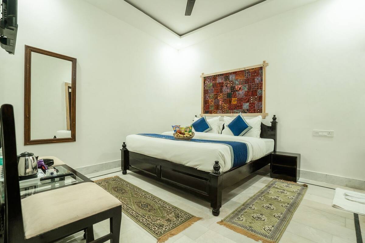 A bedroom with a bed, bedside tables, a mirror, a rug, and a wall art piece.