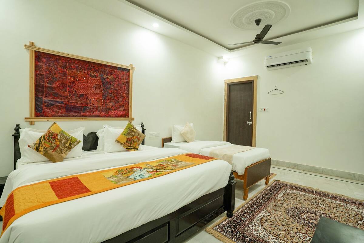 A hotel room with a large bed, two smaller beds, a ceiling fan, an air conditioning unit, and a decorative wall hanging.