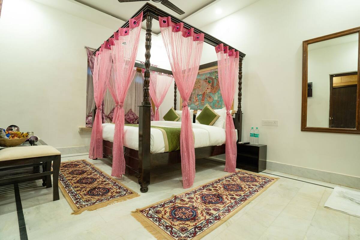 A four-poster canopy bed with pink curtains, a green pillow, and a patterned rug.