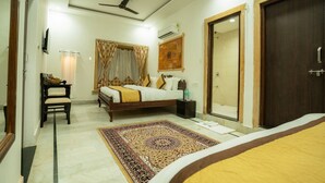 A hotel room with a bed, bedside table, chair, and a large rug. - Hotel Mantra Heritage Jaisalmer (Jaisalmer)