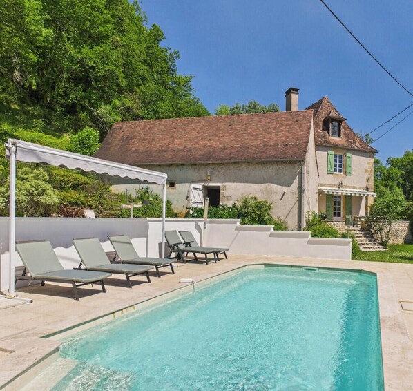 A pool area with lounge chairs and a house in the background. - Charming family home with pool - 10 guests (Thonac)