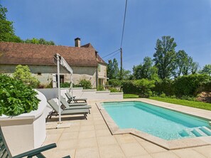 A pool area with lounge chairs and a house in the background.
