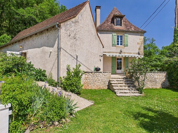 A two-story stone house with a sloped roof, a small balcony, and a stone staircase leading to the entrance.