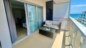 A balcony with a sofa, a glass table with a plant, and a view of the ocean.