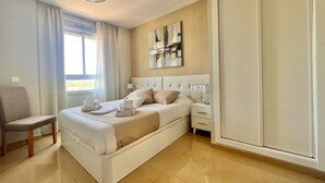 A modern hotel room with a large bed, a chair, a bedside table, and a wardrobe.