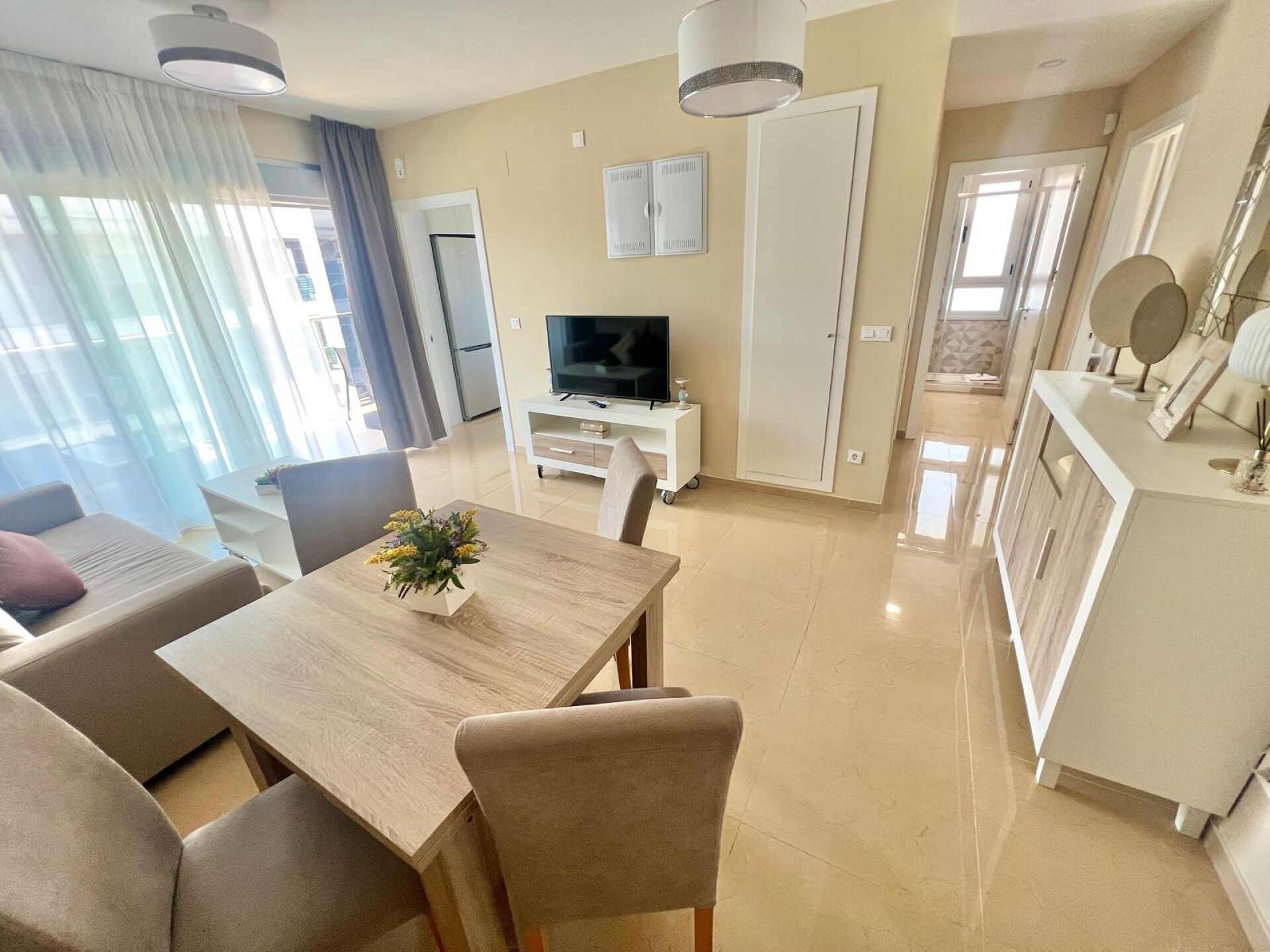 A modern living room with a dining table, sofa, TV, and kitchen area.