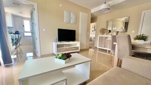 A modern living room with a flat-screen TV, a white coffee table, and a beige sofa.