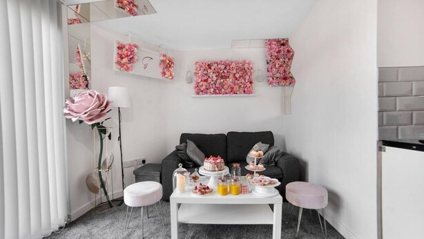 Una sala de estar moderna con un sofá gris, una mesita de centro blanca con comida y bebidas, y arreglos florales decorativos en las paredes.