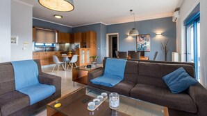 Un apartamento moderno con sala de estar, comedor y cocina. Hay dos sofás, una mesa de centro de vidrio y una mesa de comedor con sillas.