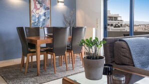 Una sala moderna con comedor, un ventanal grande que ofrece vista a la ciudad y una planta en maceta.