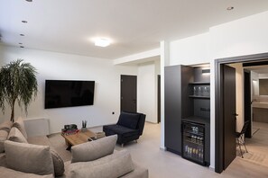 Een moderne woonkamer met een flatscreen televisie, een donkere bank, een salontafel en een grote plant.