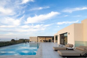 A modern outdoor pool area with a stone wall, lounge chairs, and a barbecue setup.