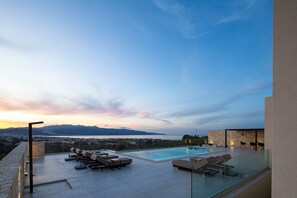 Un espace piscine aménagé sur le toit, avec des chaises longues et une balustrade en verre offrant une vue sur le paysage urbain et les montagnes.