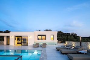A modern house with a pool, outdoor seating, and a view of the hills.
