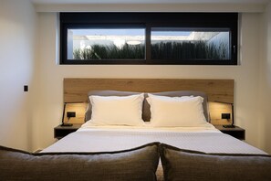 Une chambre à coucher avec une tête de lit en bois, un grand lit avec une literie blanche, deux tables de chevet avec des lampes et une fenêtre donnant sur un paysage rocheux.